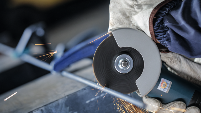PRO Metal Cutting Disc, 100 x 2.5 x 16 mm Person wearing safety equipment grinds a metal bar with a cutting tool.