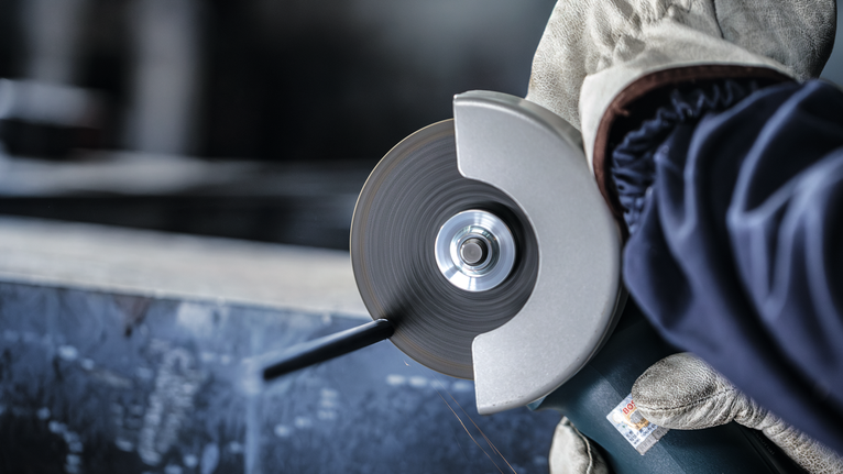 PRO Metal Cutting Disc, 100 x 2.5 x 16 mm Person wearing safety equipment uses an angle grinder to cut metal.