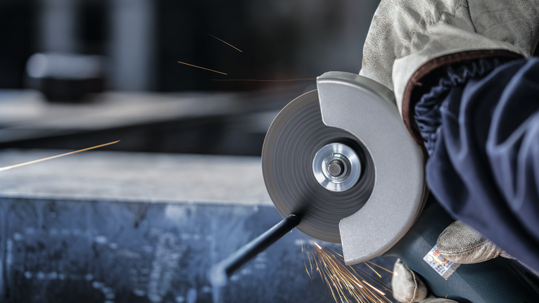 PRO Metal Cutting Disc, 100 x 2.5 x 16 mm Person wearing safety equipment cuts metal with an angle grinder, creating sparks.