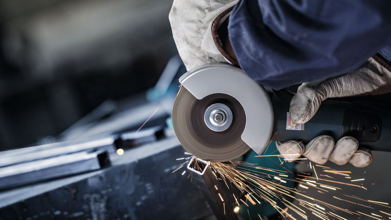 PRO Metal Cutting Disc, 100 x 2.5 x 16 mm Person wearing safety equipment uses an angle grinder to cut metal, creating sparks.