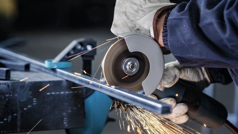 PRO Metal Cutting Disc, 100 x 2.5 x 16 mm Person wearing safety equipment cuts metal with a grinder, creating sparks.