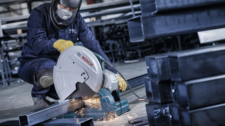 PRO Metal Cutting Disc, 355 x 3 x 25.4 mm A worker wearing safety equipment cuts metal pipes with a power saw, producing sparks.