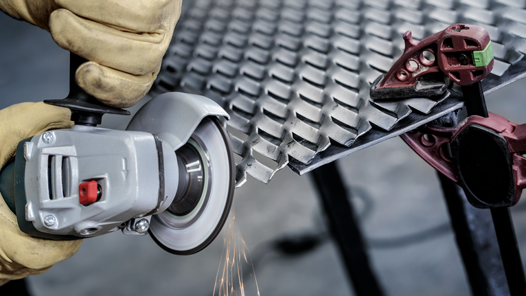 Person wearing safety equipment grinds a diamond plate with an angle grinder.