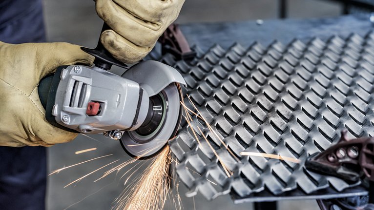 A person wearing safety equipment grinds metal diamond plate, creating sparks.