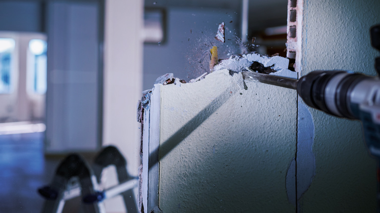 PRO SDS max-4C Flat Chisel, 25 x 600 mm Rotary hammer demolishing an interior drywall, sending debris flying.