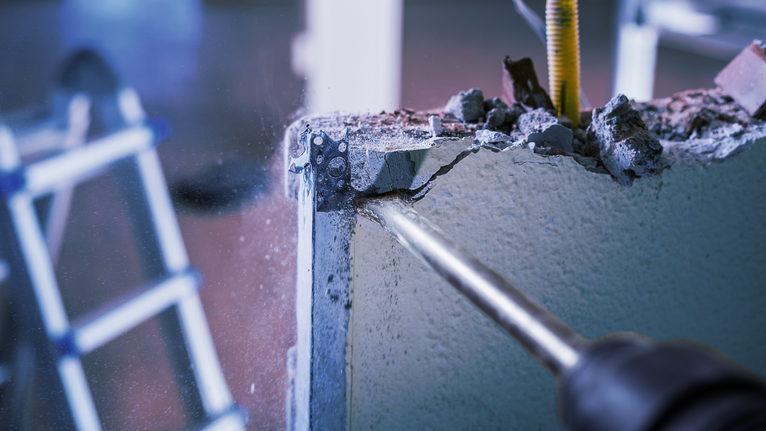 PRO SDS max-4C Flat Chisel, 25 x 600 mm Rotary hammer breaking a concrete wall corner with dust and debris flying.