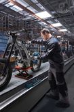 A person wearing safety equipment uses an impact driver to assemble a motorcycle frame.