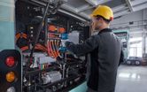 A person wearing safety equipment uses an impact wrench on an electric bus engine.