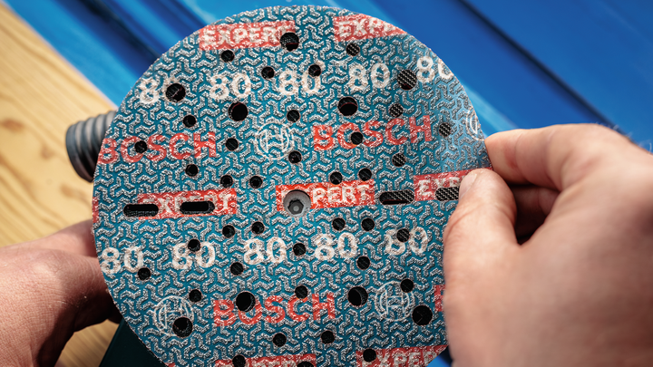 Object #200471079: 7390919_app_web_9 Person attaches a circular abrasive sanding pad onto a power sander.