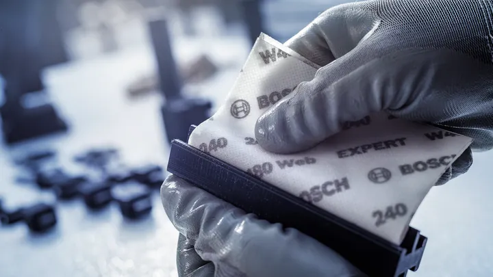 Person wearing safety equipment fits abrasive paper onto a sanding block.