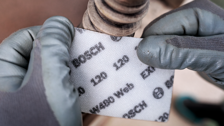 EXPERT W480 Web 1/4 Hand Sanding Sheet, 115 x 140 mm, G180 Person wearing safety equipment holds abrasive sanding pad near a metal pipe.