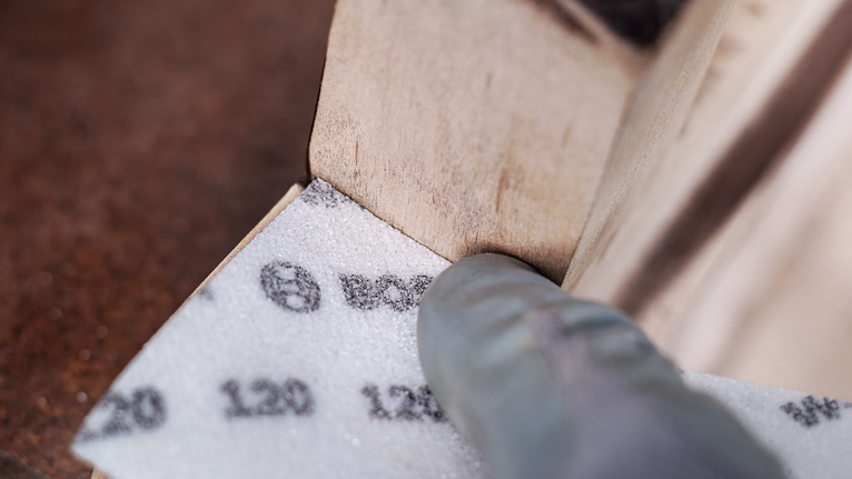 EXPERT W480 Web 1/4 Hand Sanding Sheet, 115 x 140 mm, G180 Person wearing safety equipment sanding the corner of a wooden surface.