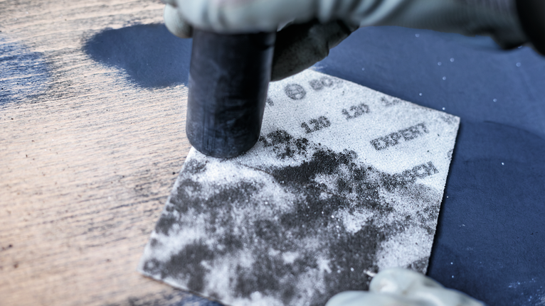 EXPERT W480 Web 1/4 Hand Sanding Sheet, 115 x 140 mm, G180 Person wearing safety equipment sanding a wooden surface with a sanding block.