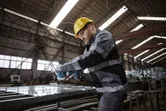 A person wearing safety equipment uses a power tool to fasten bolts on a metal frame.