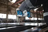 A person wearing safety equipment uses a cordless power tool to fasten screws into metal.