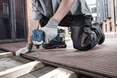 A person wearing safety equipment uses a cordless drill to fasten decking boards.