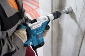 A person wearing safety equipment drills into a concrete wall with a rotary hammer.
