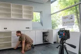 A person aligns kitchen cabinets using a laser leveling tool on a tripod.