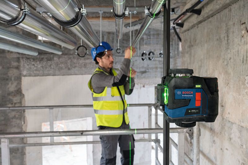 Person wearing safety equipment installs pipes using a laser leveling tool.