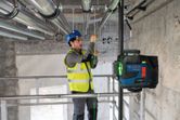 Person wearing safety equipment installs pipes using a laser leveling tool.