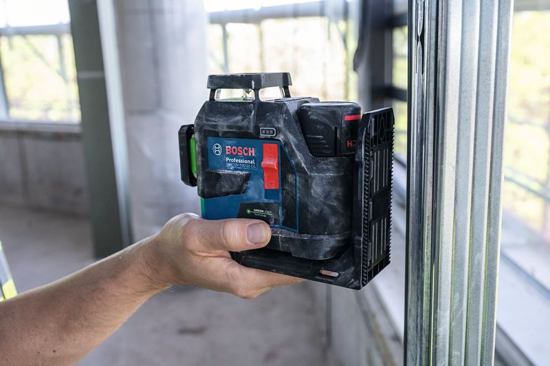A person holds a laser leveling tool against a metal frame at a construction site.