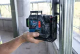 A person holds a laser leveling tool against a metal frame at a construction site.