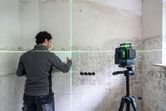 A person aligns tiles on a wall using a laser leveling tool.