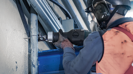 Person wearing safety equipment cuts a metal pipe with a reciprocating saw.