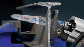 Reciprocating saw cutting through a thick metal beam in a workshop.