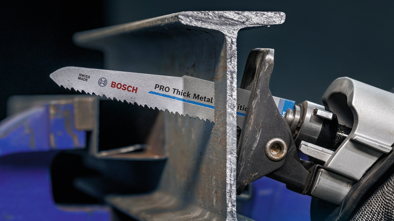Reciprocating saw cutting through a thick metal beam in a workshop.