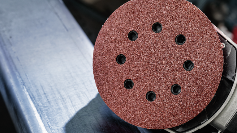 Close-up of a circular sanding pad on a power tool near a metal edge.