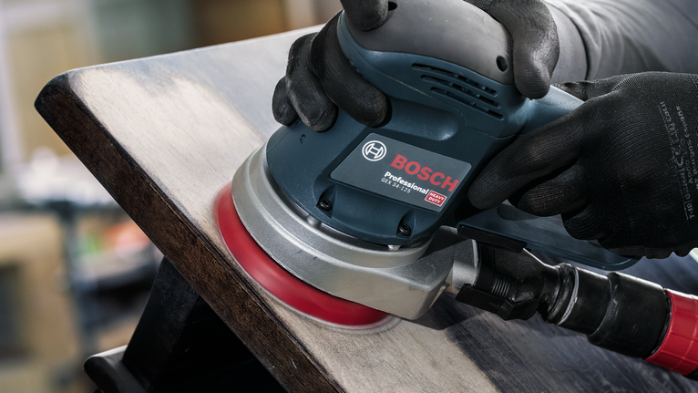 Person wearing safety equipment sands wood with an electric sander.