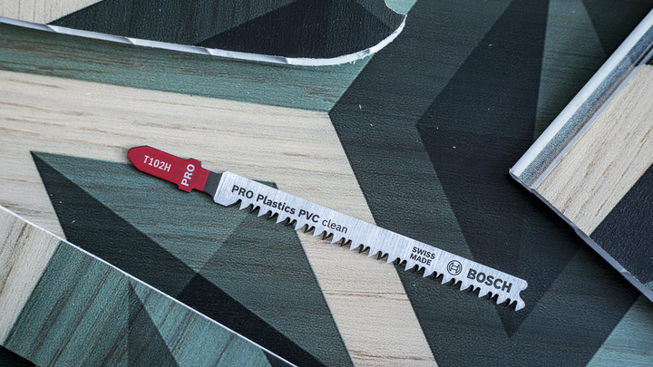 Object #200476165: 3066412_app_web_2 Jigsaw blade lying on patterned wood and plastic sheet surfaces.