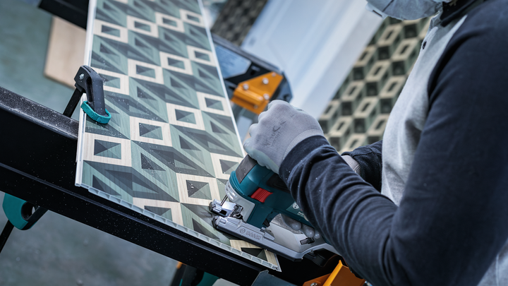Object #200476168: 3066412_app_web_5 Person wearing safety equipment uses a jigsaw to cut patterned wood panel.