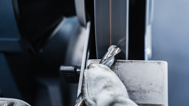 PRO Metal Grinding Wheel, 150 x 20 x 20 mm, G24 Person wearing safety equipment sharpening a metal drill bit on a bench grinder.