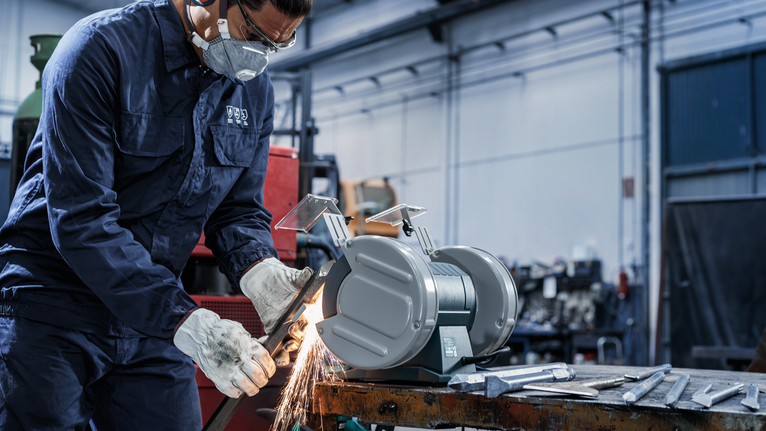 PRO Metal Grinding Wheel, 150 x 20 x 20 mm, G24 Person wearing safety equipment grinds metal using a stationary grinder in a workshop.
