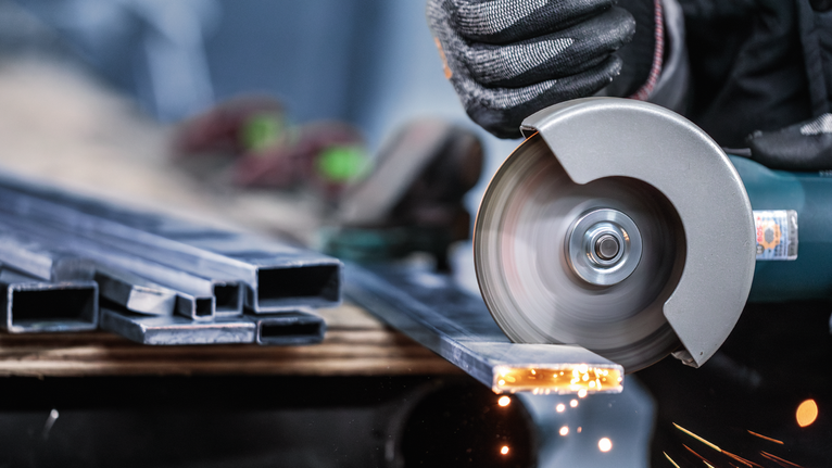 PRO Stainless Steel and Metal Cutting Disc, 125 x 1 x 22.23 mm A person wearing safety equipment cuts metal profiles with an angle grinder.