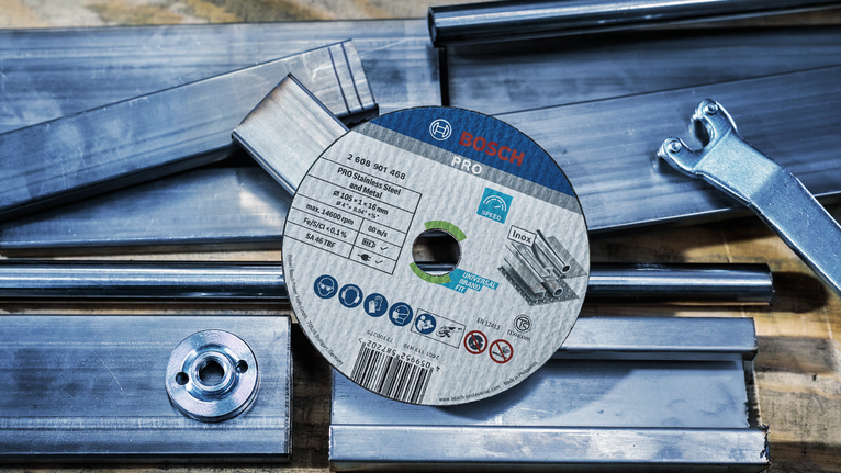 PRO Stainless Steel and Metal Cutting Disc, 125 x 1 x 22.23 mm Cutting disc lying on metal bars next to a wrench on a workbench.