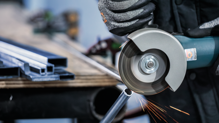 PRO Stainless Steel and Metal Cutting Disc, 125 x 1 x 22.23 mm Person wearing safety equipment cuts a metal pipe with an angle grinder.