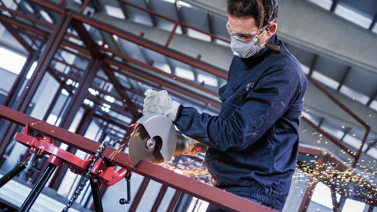 PRO Metal Cutting Disc, 180 x 3 x 22.23 mm A person wearing safety equipment uses a power cutter to cut a metal pipe, producing sparks.