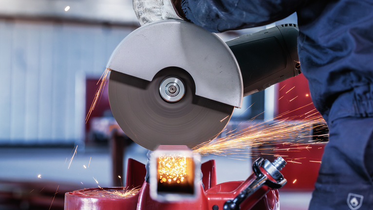 PRO Metal Cutting Disc, 180 x 3 x 22.23 mm Person wearing safety equipment uses an angle grinder to cut metal, creating sparks.