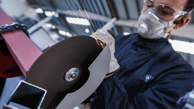 PRO Metal Cutting Disc, 180 x 3 x 22.23 mm Person wearing safety equipment cuts metal with a spinning angle grinder.