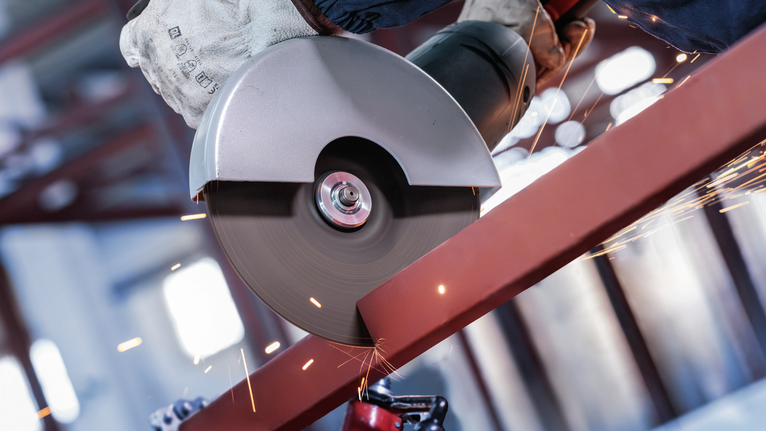 PRO Metal Cutting Disc, 180 x 3 x 22.23 mm A person wearing safety equipment cuts a metal beam with a circular saw.