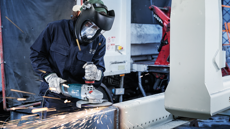 PRO Stainless Steel Grinding Disc, 100 x 6 x 16 mm A person wearing safety equipment uses an angle grinder to cut a metal beam.