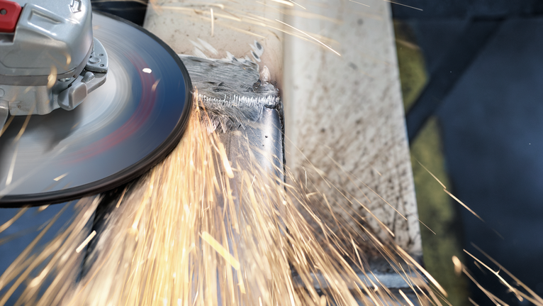 PRO Stainless Steel Grinding Disc, 100 x 6 x 16 mm Angle grinder creating sparks while cutting a metal beam.