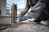 A person wearing safety equipment grinds rebar on a construction site, creating sparks.