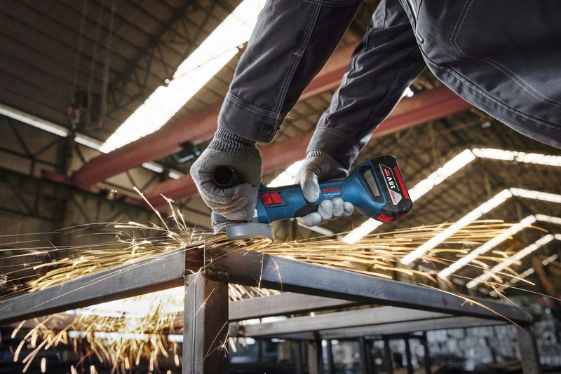 A person wearing safety equipment grinds a metal beam with an angle grinder.