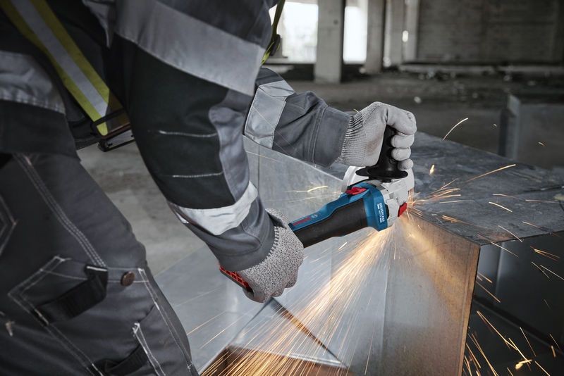 A person wearing safety equipment grinds a metal slab, producing bright sparks.