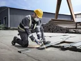 A worker wearing safety equipment cuts metal with a power grinder at an industrial site.