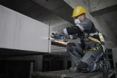 A person wearing safety equipment grinds concrete with a power tool on a construction site.